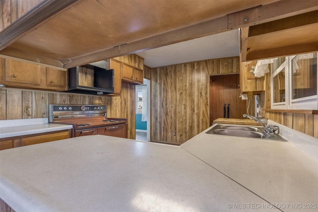 kitchen with range with electric cooktop, a sink, wooden walls, brown cabinetry, and light countertops