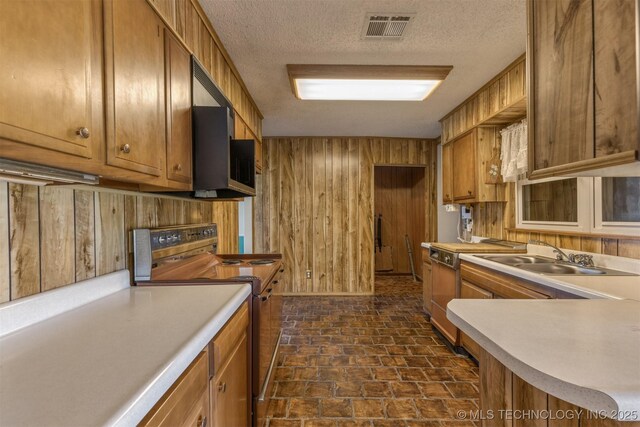 kitchen featuring electric range, a sink, wooden walls, brown cabinetry, and light countertops