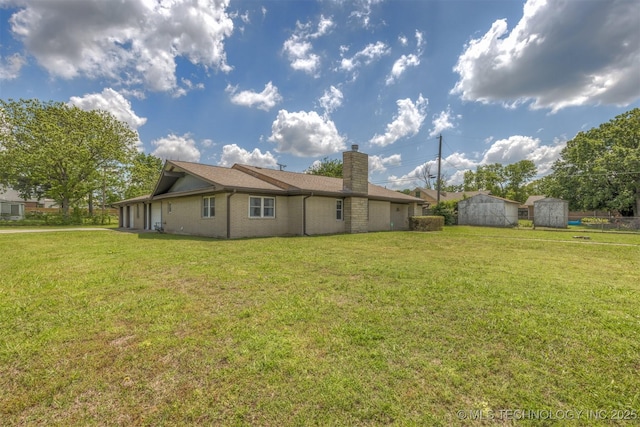 back of house featuring a chimney, a storage shed, a lawn, and an outdoor structure