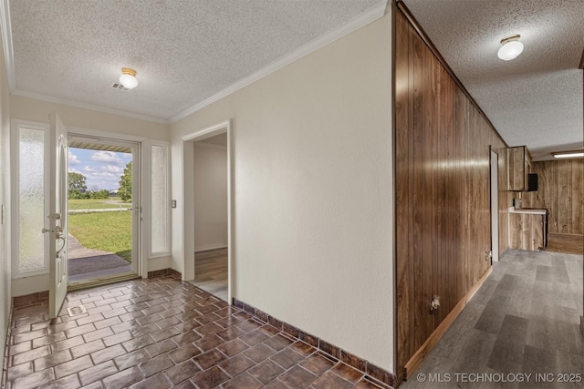 foyer with a textured ceiling, wooden walls, baseboards, and crown molding