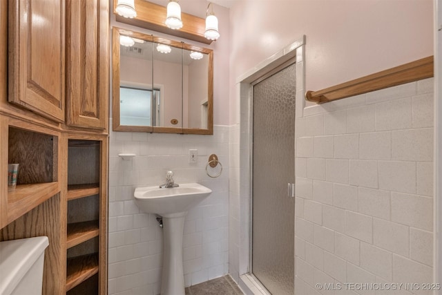 full bathroom with a stall shower, tile walls, toilet, wainscoting, and a sink