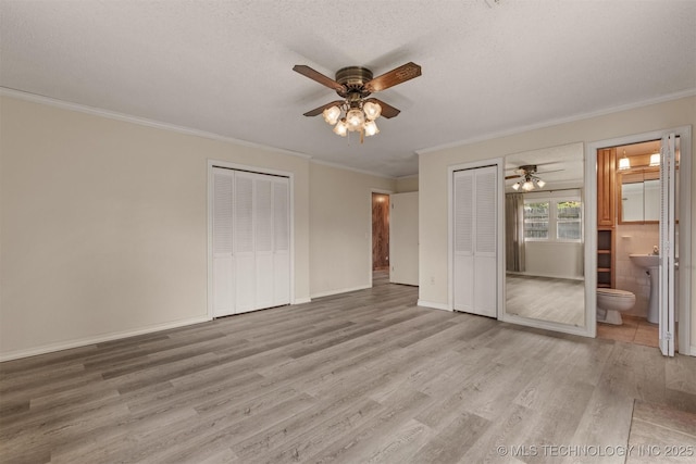 unfurnished bedroom with two closets, crown molding, wood finished floors, ensuite bath, and a textured ceiling
