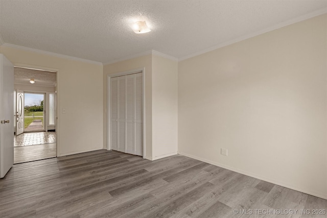 empty room featuring a textured ceiling, wood finished floors, crown molding, and baseboards
