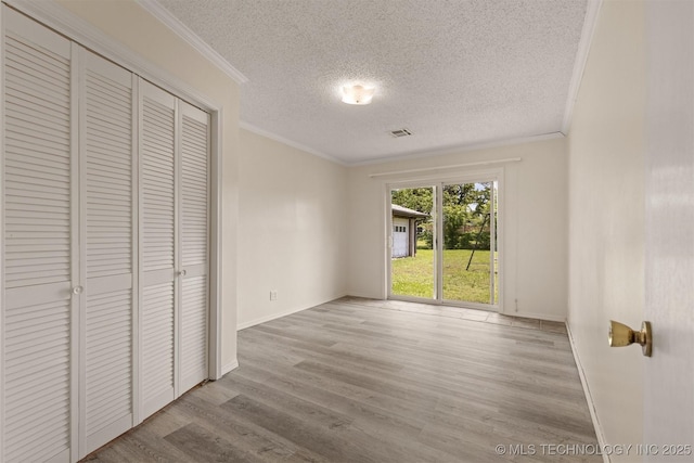 unfurnished bedroom with a textured ceiling, crown molding, access to exterior, wood finished floors, and baseboards