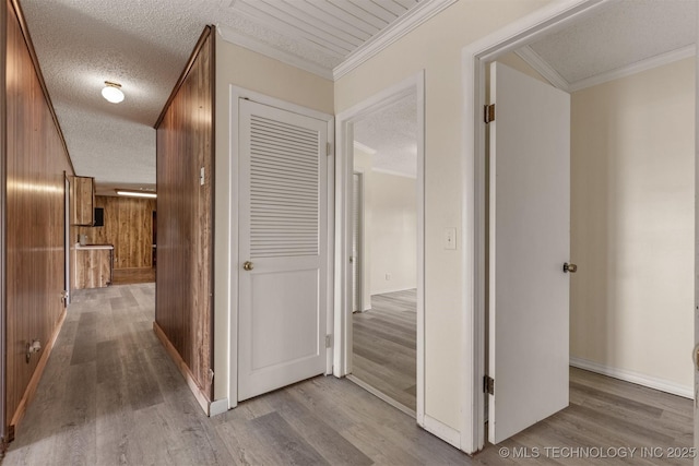 hallway with wood finished floors, wood walls, ornamental molding, a textured ceiling, and baseboards