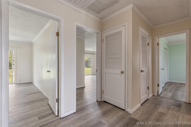 hall with wood finished floors, plenty of natural light, a textured ceiling, crown molding, and baseboards