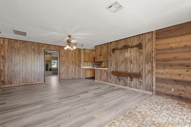 unfurnished living room with a ceiling fan, wooden walls, a textured ceiling, light wood-type flooring, and baseboards