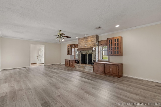 unfurnished living room featuring a textured ceiling, ornamental molding, a brick fireplace, a ceiling fan, and light wood-style flooring