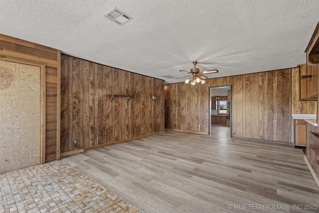 unfurnished living room featuring wooden walls, a ceiling fan, wood finished floors, and a textured ceiling