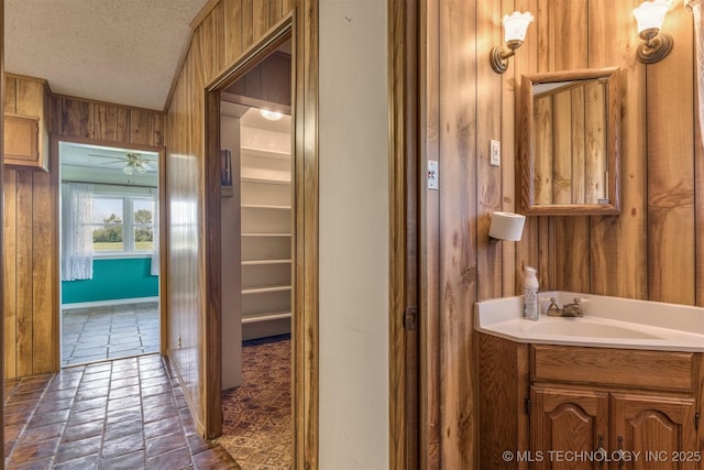 bathroom featuring wood walls, a textured ceiling, vanity, and ceiling fan