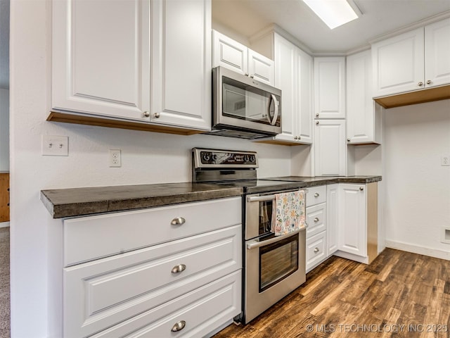 kitchen with appliances with stainless steel finishes, dark countertops, white cabinets, dark wood finished floors, and baseboards