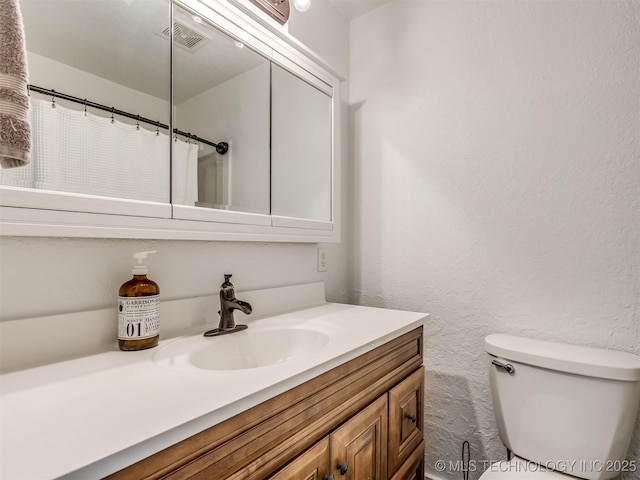 full bath with vanity, toilet, and a textured wall