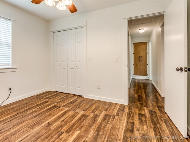 unfurnished bedroom with attic access, wood finished floors, a closet, and baseboards