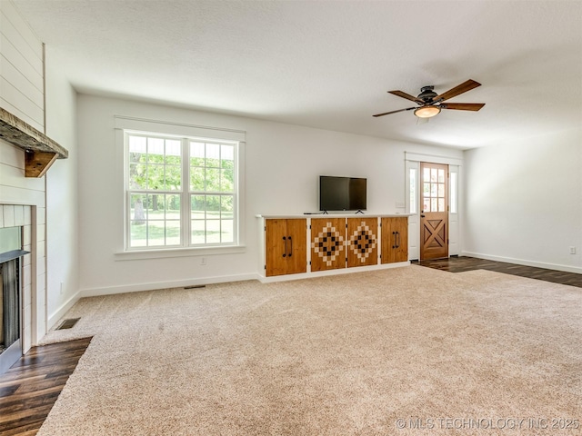 unfurnished living room featuring a fireplace, a ceiling fan, baseboards, and dark colored carpet