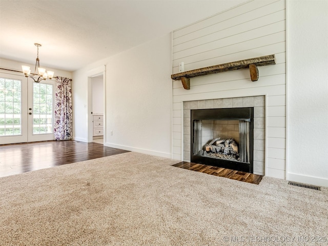 unfurnished living room featuring carpet floors, a chandelier, baseboards, a tile fireplace, and french doors