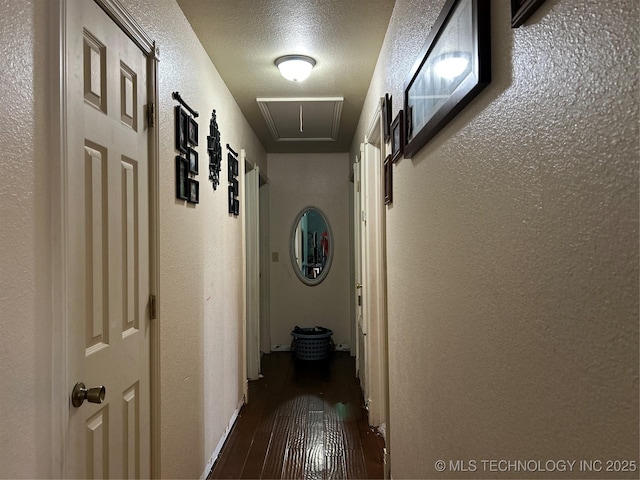 hall with attic access, a textured wall, and dark wood-type flooring