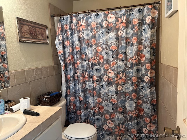 bathroom with tile walls, vanity, toilet, a textured wall, and a shower with curtain