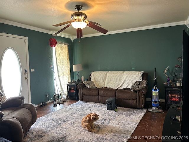 living room with a ceiling fan, wood finished floors, crown molding, and a wood stove