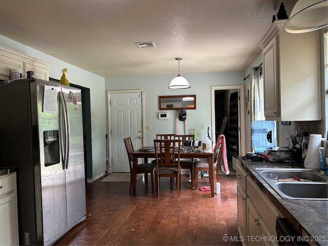 kitchen with stainless steel refrigerator with ice dispenser, dark countertops, a sink, dark wood-style flooring, and a textured ceiling