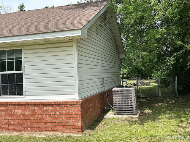 view of property exterior with central AC unit, brick siding, a gate, a shingled roof, and fence