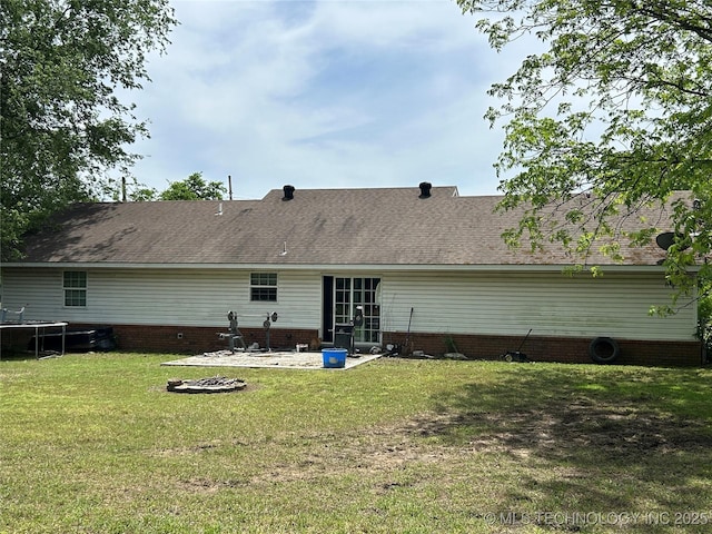 rear view of property with a trampoline, a patio area, a yard, and a shingled roof