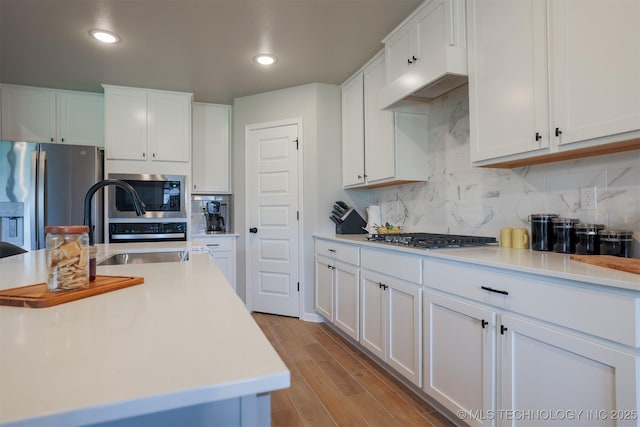 kitchen with stainless steel appliances, light countertops, white cabinetry, light wood-style flooring, and decorative backsplash