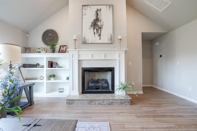 living room featuring light wood-style floors, a fireplace with raised hearth, baseboards, and high vaulted ceiling