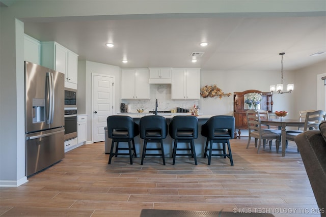 kitchen with appliances with stainless steel finishes, a chandelier, light wood-style flooring, decorative backsplash, and recessed lighting