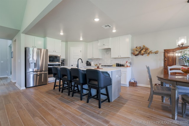kitchen featuring appliances with stainless steel finishes, a kitchen bar, light countertops, white cabinets, and light wood-type flooring
