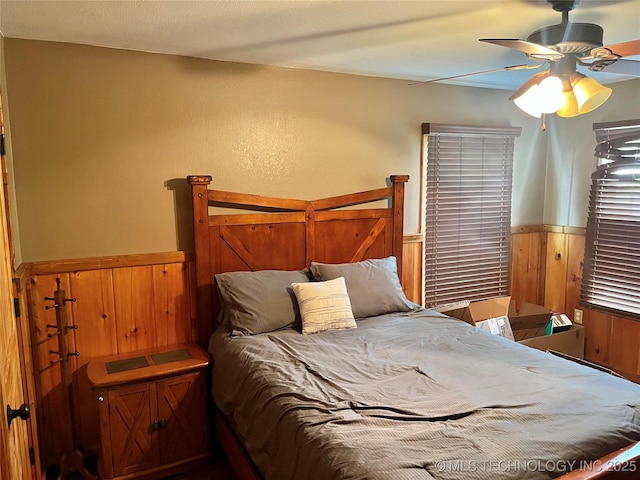 809 N K St, Quinton, OK 74561 - bedroom featuring wainscoting, wood walls, and a ceiling fan