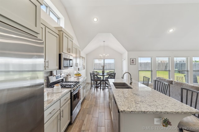 kitchen featuring stainless steel appliances, a sink, lofted ceiling, an island with sink, and a chandelier