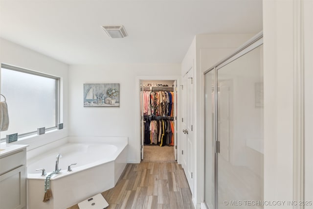 full bathroom with a stall shower, a garden tub, wood finished floors, vanity, and a walk in closet