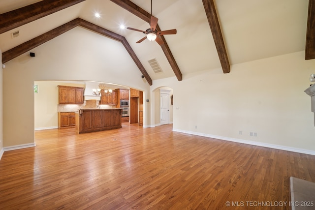 7287 E 111th Pl, Bixby, OK 74008 - unfurnished living room featuring arched walkways, a ceiling fan, beamed ceiling, high vaulted ceiling, and light wood-style flooring