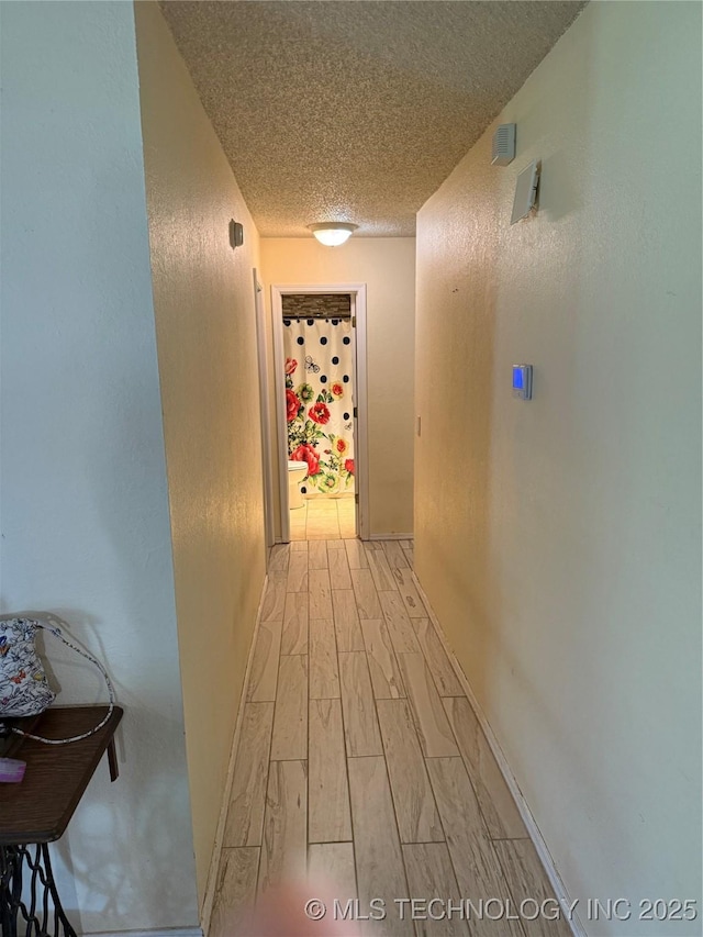corridor featuring a textured ceiling, a textured wall, light wood-style floors, and baseboards