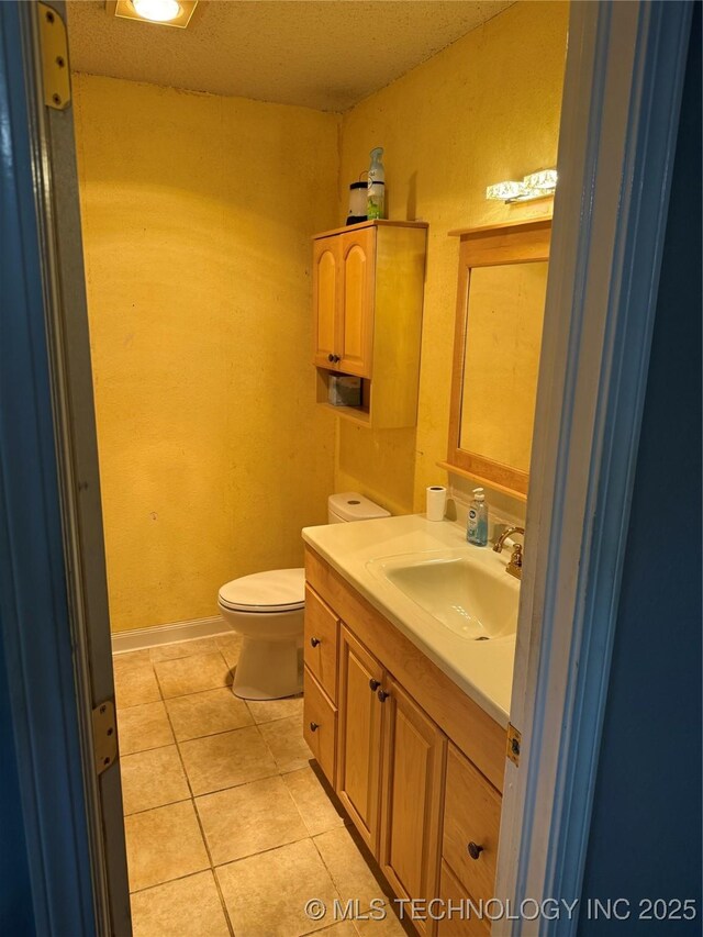 half bathroom with tile patterned flooring, toilet, vanity, and baseboards