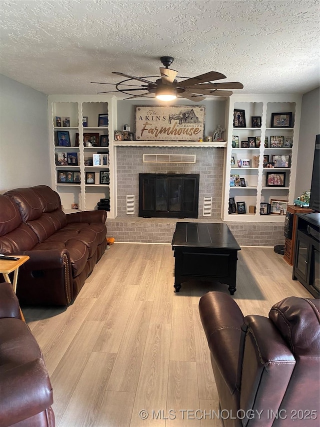 living room with a ceiling fan, a textured ceiling, wood finished floors, built in shelves, and a brick fireplace