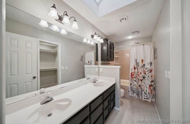 bathroom with wood finished floors, toilet, shower / bath combo with shower curtain, a skylight, and double vanity