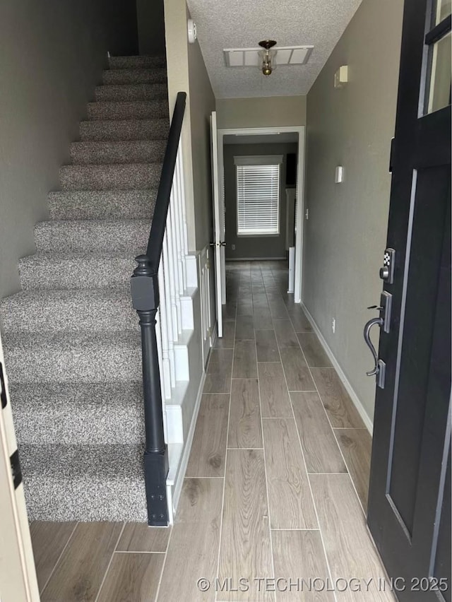 staircase with wood tiled floors, a textured ceiling, and baseboards