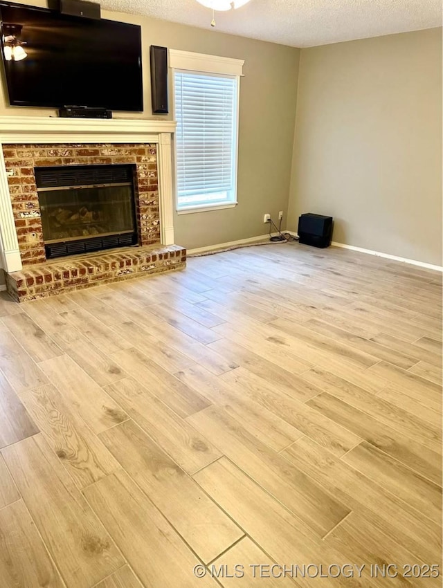 unfurnished living room with wood finished floors, baseboards, a textured ceiling, and a fireplace