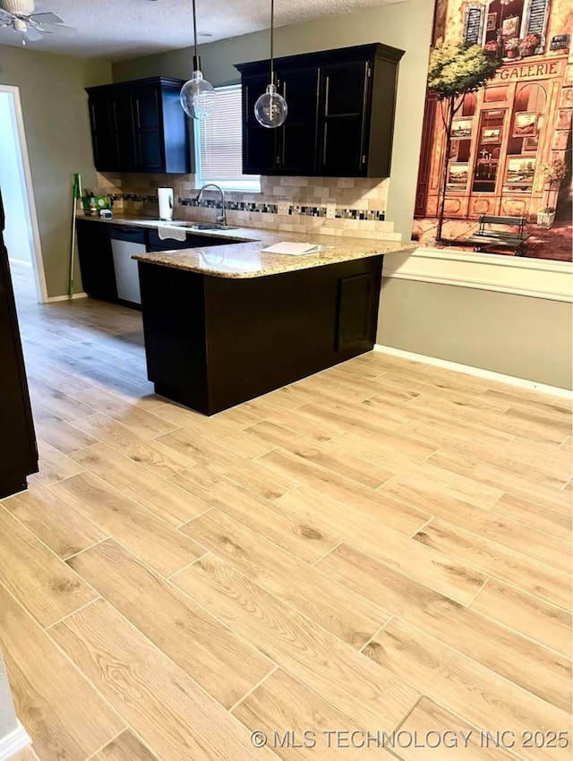 kitchen featuring a peninsula, dark cabinets, light wood finished floors, a sink, and backsplash