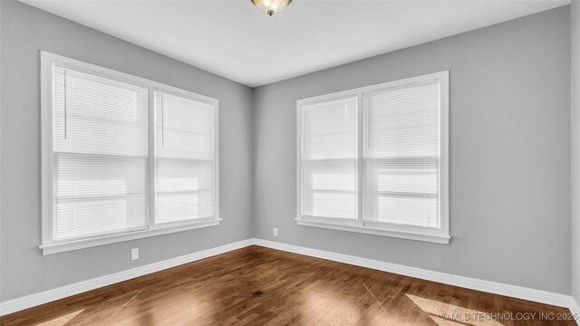 711 N SW, Ardmore, OK 73401 - unfurnished room featuring baseboards, healthy amount of natural light, and dark wood-type flooring