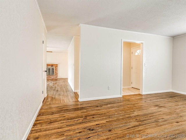 unfurnished room featuring ornamental molding, wood finished floors, a textured ceiling, baseboards, and a brick fireplace