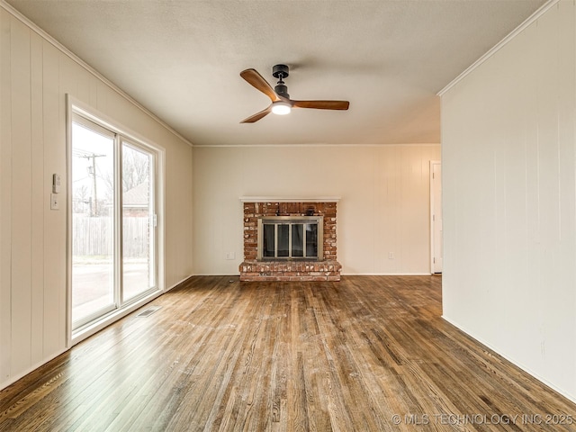 unfurnished living room featuring hardwood / wood-style flooring, ornamental molding, a ceiling fan, a brick fireplace, and wood walls