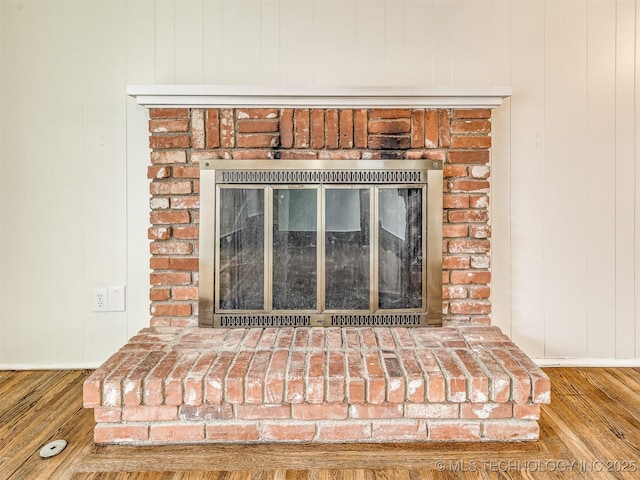 detailed view of wood finished floors, baseboards, and a brick fireplace