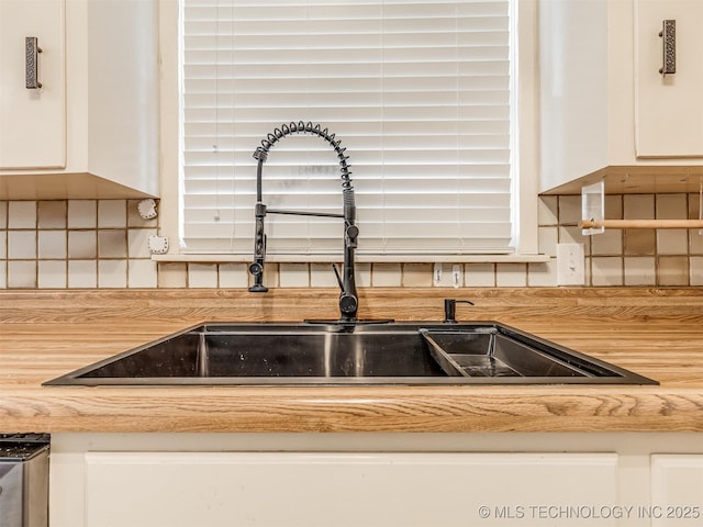kitchen view of a sink, white cabinets, and decorative backsplash