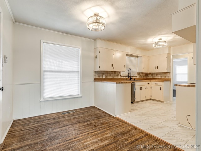 kitchen featuring a sink, light wood-style flooring, wainscoting, white cabinets, and decorative backsplash