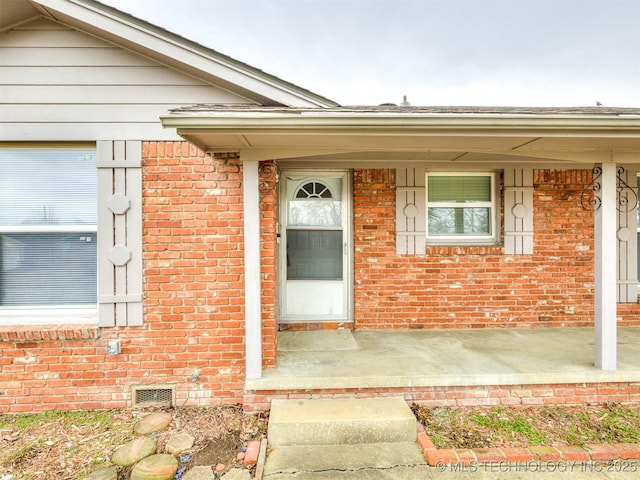 entrance to property with brick siding, a porch, and crawl space