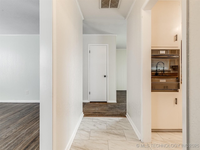 hallway with ornamental molding, marble look tile flooring, and baseboards