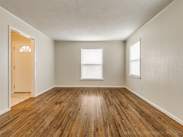 spare room with crown molding, wood finished floors, a textured ceiling, and baseboards