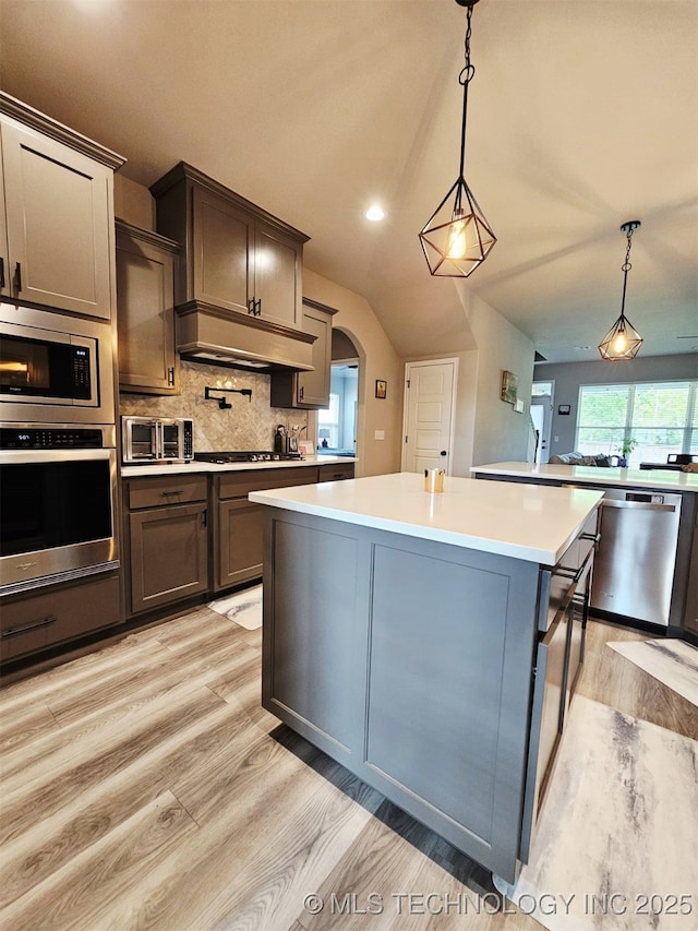 kitchen with stainless steel appliances, light wood-style flooring, a center island, decorative backsplash, and light countertops